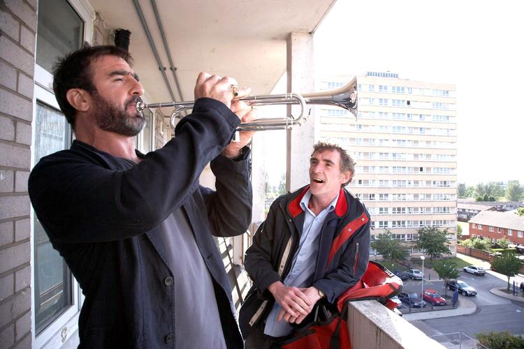 Det lille postbud Eric (th.) forguder den store fodboldstjerne Eric. Cantona viser sig dog også at være et menneske, da han demonstrerer, at han ikke helt fik lært at spille trompet under en af sine karantæner fra Manchester United. Foto fra filmen. 