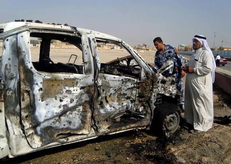 Folk ved en ødelagt bil efter bombeangreb i Ramadi, der ligger 115 kilometer vest for hovedstaden Bagdad. 