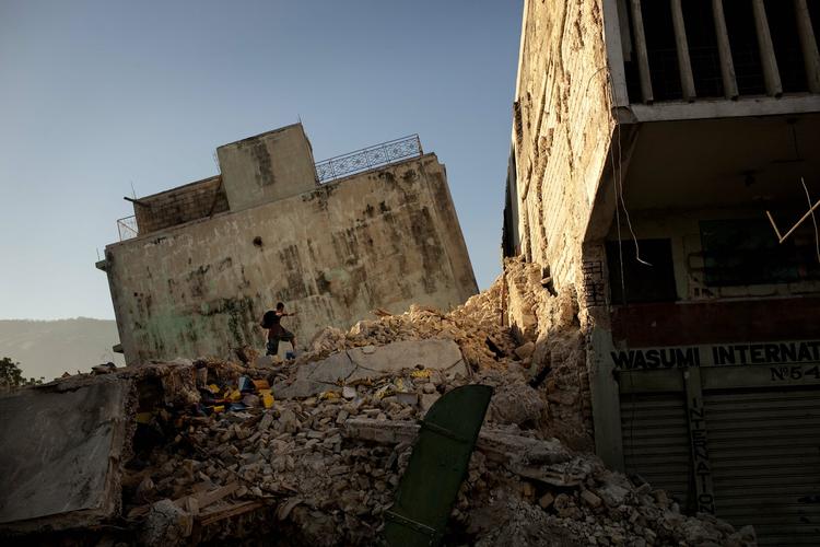 En mand står på toppen af en sammenstyrtet bygning i Port-au-Prince. 