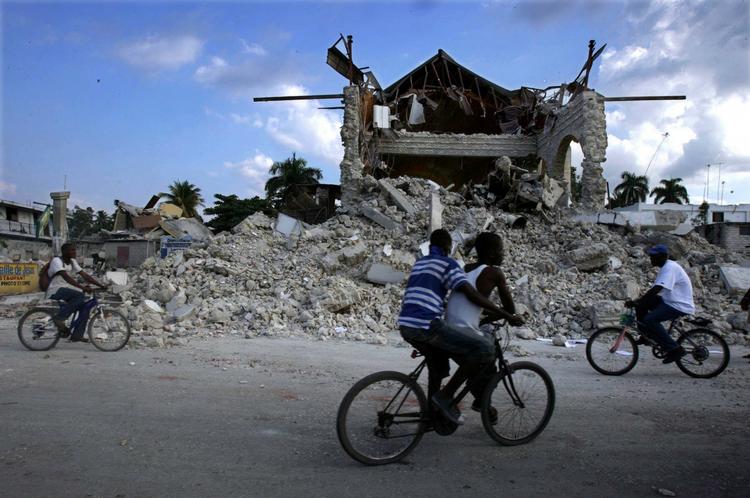 ødelæggelser. Cyklister ved den ødelagte kirkegård i Leogane i Haiti. 