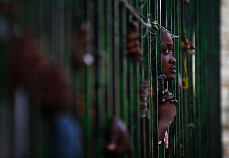 nødhjælp. En kvinde kigger gennem tremmerne på et hegn, mens hun betragter uddeling af mad i Haiti 