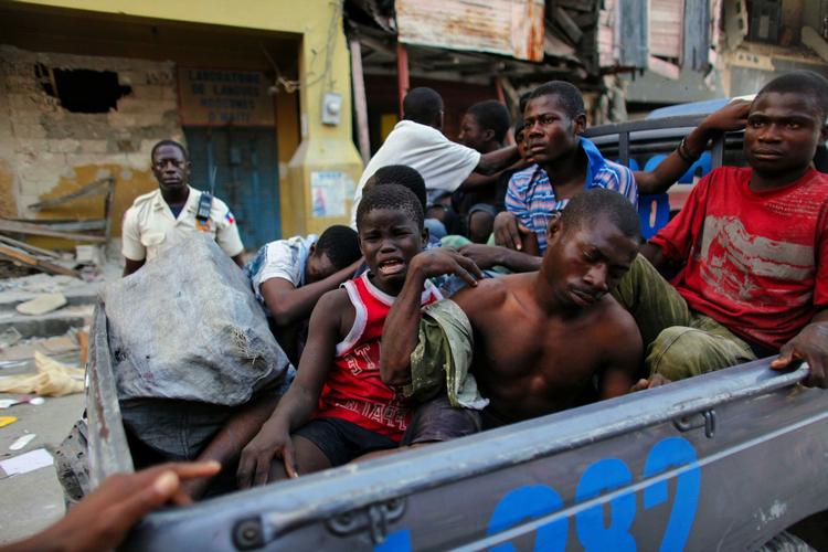 En politimand gør klar til at køre en gruppe haitianere væk - herunder et barn - der er arresteret for at plyndre i ruinerne. 