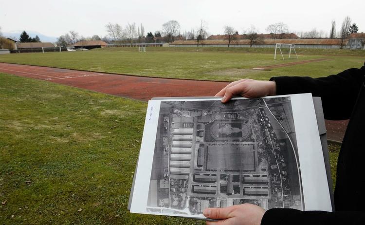 Begravelsesplads. Det østrigske forsvar har offentliggjort dette billede, hvor en mand holder et luftfoto taget af amerikanske piloter frem. På billedet kan man angiveligt se åbne massegrave, hvor der i dag er en fodboldbane, som man kan se det i baggrunden. 