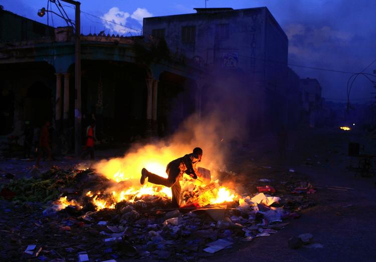 ødelagt. En indbygger i det centrale Port-au-Prince putter brænde på et bål, der skal holde myggene væk fra de mange, der må overnatte i det fri. 