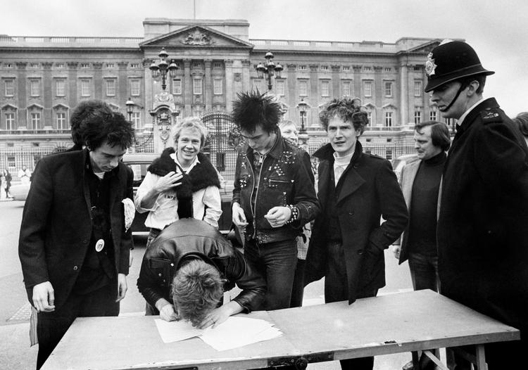 JUBILÆUM. Med vanlig sans for virkningen af provokation valgte Malcolm McLaren (nr. 3 fra højre), at Sex Pistols skulle udgive sin anden single 'God Save the Queen' samtidig med dronning Elizabeths 25-års jubilæum på tronen i 1977. Her skriver bandet kontrakten under foran Buckingham Palace. Manageren blev selv anholdt, da Sex Pistols spillede sangen live på en båd på Themsen ud for det britiske parlament. Men strategien virkede - singlen indtog 1. pladsen. Arkivfoto: AP 
