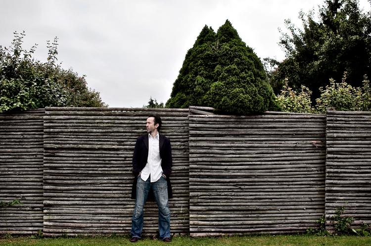 Da Kim Fupz Aakesons familie flyttede til Albertslund, var byen først lige ved at blive til. Men blev det på en måde aldrig. Alt var perfekt i den nye verden, men for Kim var det en ørken. Her står han ved sin barndomshaves raftehegn, som også ses på barndomsbilledet nedenfor. Foto: Miriam Dalsgaard 