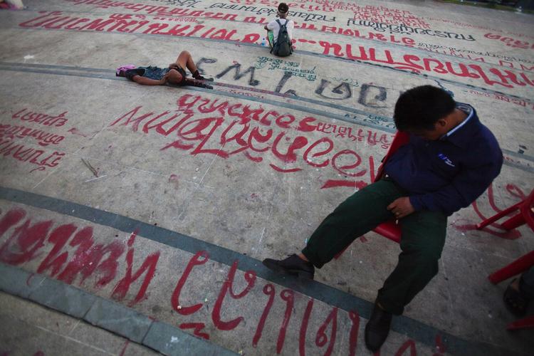 VENTETID. Thaier tager et hvil nær demokratimonumentet i Bangkok, hvor vejbelægningen er fyldt med anti-regerings-grafitti. 