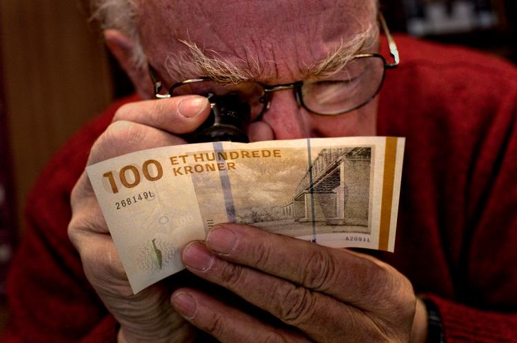 Mønthandler Peter Flensborg har luppen fremme, da den nye hundredkroneseddel studeres for første gang. Foto: Per Folkver 