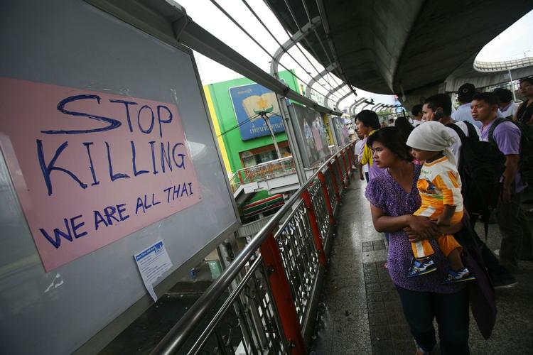 UDKIGSPOST. Forbipasserende kigger ned på rødskjorternes demonstrationer i det indre Bangkok. 