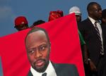 Kandidat. En fan holder et banner med Wyclef Jean mens rapperen selv, til højre, forlader et valgkontor i Port-au-Prince, hvor han officielt har erklæret sig som præsidentkandidat. 