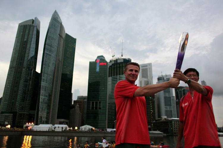 Ildsjæle. Den mangedobbelte verdensmester i stangspring, Sergei Bubka (tv.) overtager den olympiske fakkel fra Eugene Heng foran Singapores skyline. 