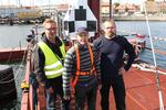 Lækkerier. Enkelte småting skal stadig klares på havnen, og så er det jo godt, når en venlig sjæl forærer raketmændene en æske lakridspiber. De var i hvert fald meget taknemmelige. Til højre: Steen Andersen, it-arkitekt og frivillig på projektet, i midten: Kristian Von Bengtson, den ene af de to hovedraketmænd, til højre: En endnu ukendt raketmand. 