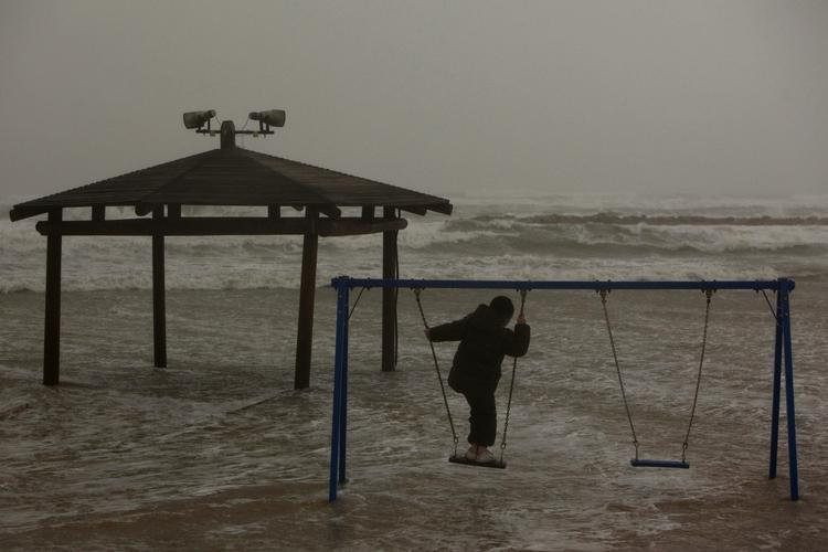 bølger. Et barn i Tel Aviv har trodset elementernes rasen og leger på stranden. 