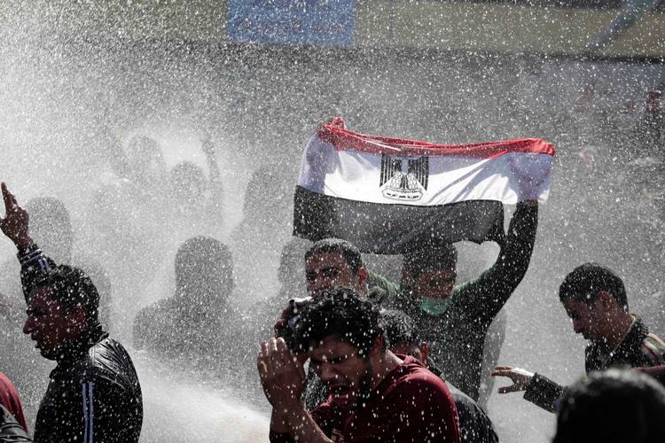En egyptisk demonstrant holder det egyptiske flag op foran politistyrker, der bruger vandkanoner mod demonstranterne i Kairo. 