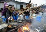 Overlevende fra tsunamien og jordskælvet laver mad over åben ild foran deres ødelagte hus i Ishinomaki. 