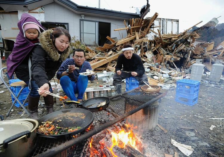 Overlevende fra tsunamien og jordskælvet laver mad over åben ild foran deres ødelagte hus i Ishinomaki. 