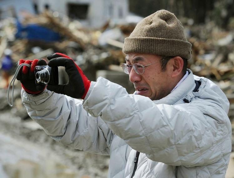En mand græder mens han tager billeder af sit ødelagte hjem i Minamisanriku. 