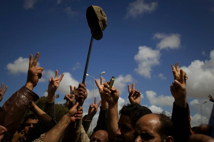 Libyske oprørere jubler i udanten af oprørsbyen Benghazi. På pinden hænger en kasket fra en Gaddafi-loyal soldat. 