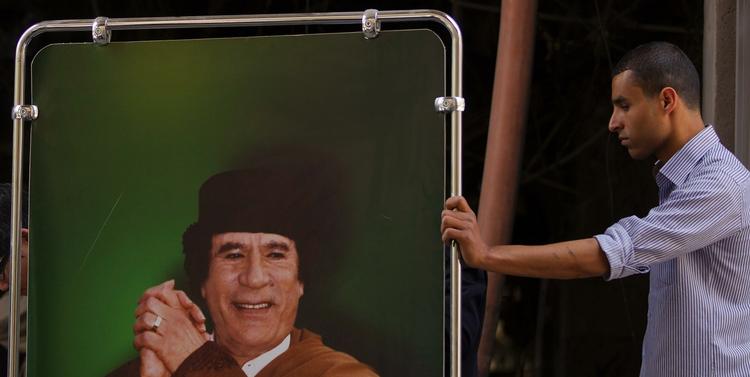 Rulletur. Gaddafi-styret tager ofte journalister med på guidede ture efter Natobombardementer. Billedet er fra maj, hvor en mand ruller en plakat af lederen ind i en bygning, som var blevet bombet. 