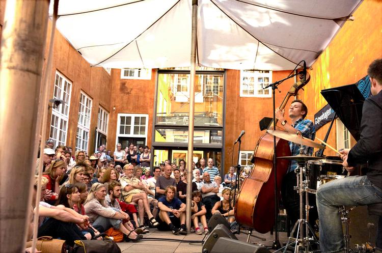 Tvetydigt. Man sidder ude i Kunstforeningens gård, men det føles grangiveligt som inde.