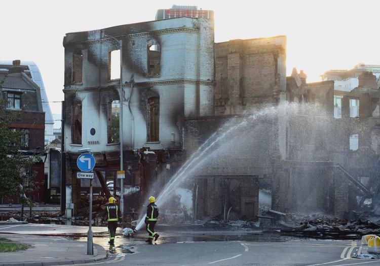 ramt. Brandfolk slukker den sidste ild i en udbrændt bygning i London-bydelen Croydon. Det var her, at en 26-årig mand blev skudt og senere døde af sine kvæstelser. 