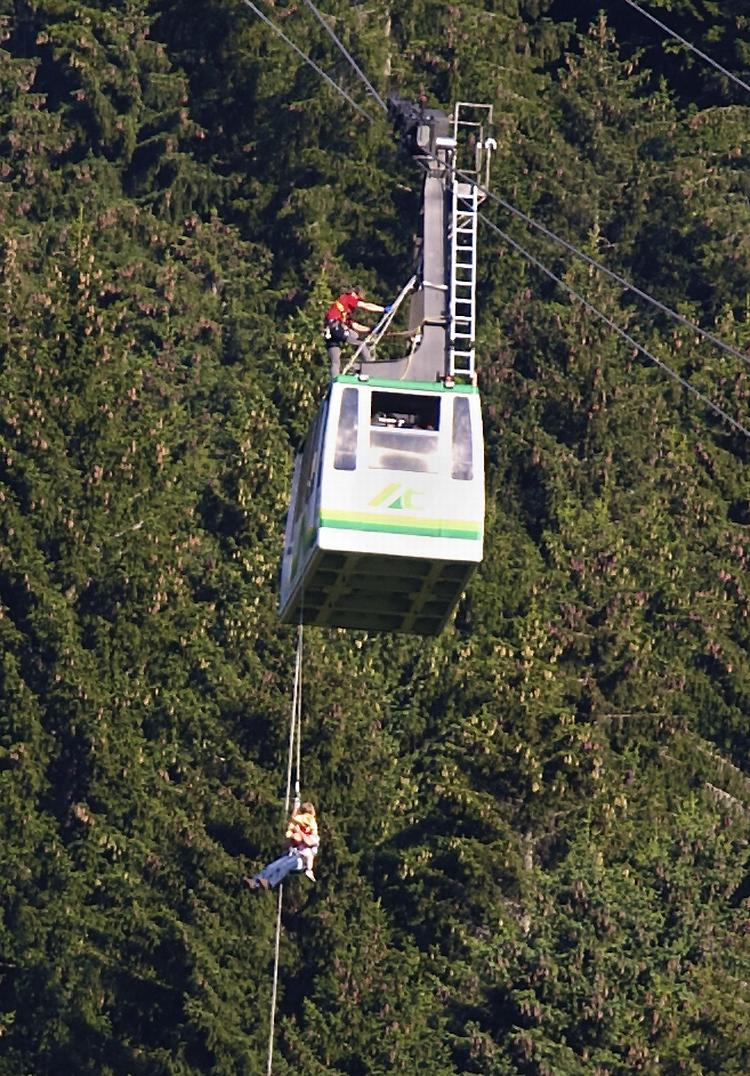 FANGET. Turister sad fast i alperne, da en paraglider styrtede ind i kablerne i går. Her hjælpes passagerer ned fra 50-meters højde. Yderligere 20 mennesker måtte vente en hel nat, før de kunne komme ned fra deres kabelbil,som var fanget i 80-meters højde. 