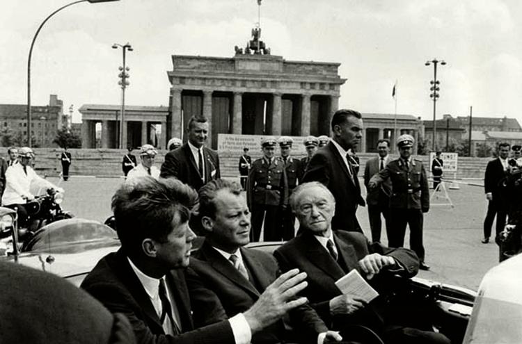Møde. USA's Præsidentnt John F. Kennedy (tv)  den daværende borgmester for Vestberlin Willy Brandt og den vesttyske kansler Konrad Adenauer i bil ved Brandenburg  26. juni  1963. 