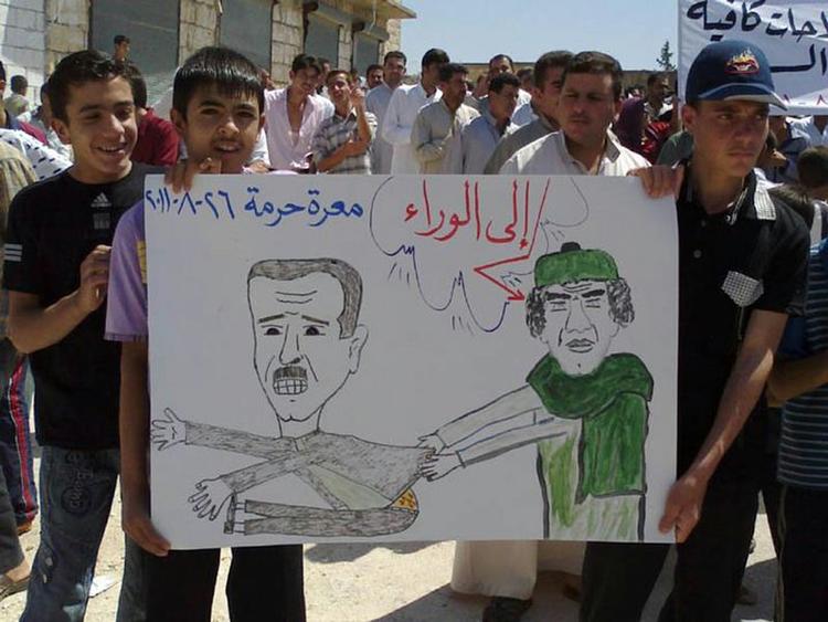 oprør. Dette billede stammer ifølge aktivister fra en demonstration i landsbyen Harma, hvor drenge fremviser en tegning af Syriens præsidents Bashar Assad (tv.) og Libyens Moamar Gaddafi med ordene: 'Træd tilbage'. 
