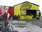 Spot. Cykelsmeden Baisikelis mur er udsmykket af den amerikanske kunstner Shepard Fairey og spiller skarpt op til forretningen kanariegule facade med cafeborde og et væld af cykler parkeret foran. 