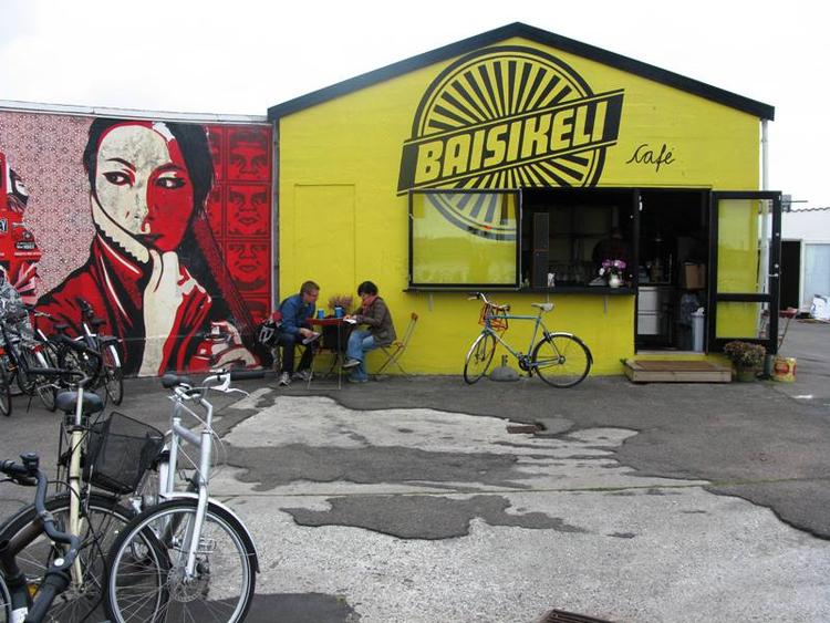 Spot. Cykelsmeden Baisikelis mur er udsmykket af den amerikanske kunstner Shepard Fairey og spiller skarpt op til forretningen kanariegule facade med cafeborde og et væld af cykler parkeret foran. 