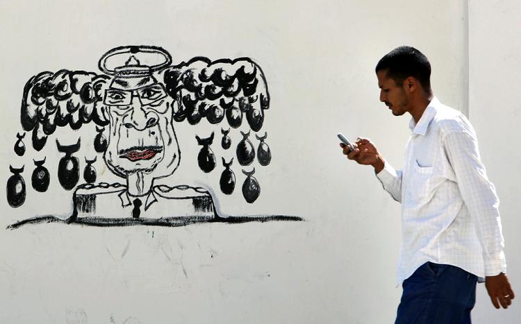 Satire. Tripoli i går. En mand passerer en graffiti med Libyens afsatte diktator, Moamar Gaddafi, som gemmer sig et eller andet sted. 