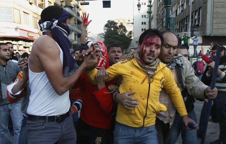 Kamp. Demonstrerende på Tahrir-pladsen i Kairo hjælper en såret mand. Kampene sker kun 9 dage før de første demokratiske valg i landet siden Hosni Mubarak gik af som præsident. 