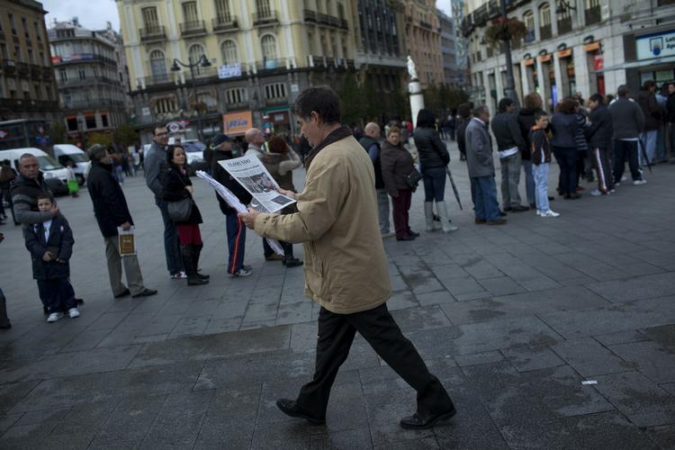 Lottogevinst? En mand læser om det kommende valg i avisen. Bag ham står køer med spaniere, der er mere interesseret i at få fat i en lottokupon - og gerne én med gevinst på. De har ikke nogen særlig tiltro til, at en ny regering kan ændre deres situation med arbejdsløshed. 
