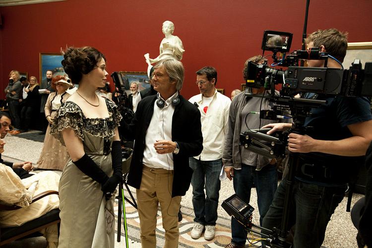 Stille styring. I vrimlens centrum glider en solbrændt Bille August omkring med et sæt hovedtelefoner om halsen. Afslappet klædt i sort blazer, lys skjorte, kakibukser og hvide Nikesko styrer han slagets gang og konfererer sagte med sine medarbejdere. Fra tid til anden lægger han blidt hånden på en skuespillers arm eller skulder. Før hver indstilling håndplukker han statister fra mængden og flytter lidt rundt på dem. Sekunder før klaptræet smælder, opdager han, at en gentleman i baggrunden har glemt at fjerne sine briller fra næsen, og sender diskret sin assistent af sted for at rette fejlen. 