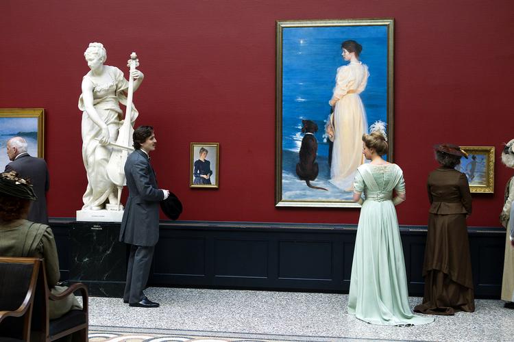 En ægte Krøyer? For 120 år siden udstillede Carl Jacobsen sin enorme kunstsamling i disse sale, inden bryggersønnen flyttede klenodierne til det større Ny Carlsberg Glyptotek. Men denne ene dag i 2011 får kunsten atter lov at indtage konferencelokalerne i Carlsberg Museum. Filmens budget på 22 mio. kr. rækker dog ikke til ægte Krøyere i billedrammerne. Først når man stikker snuden helt tæt på de ophængte malerier, afsløres rasterstrukturen i reprotrykkene. Korridoren bugner af sminkeborde, spejle, kravatter, flipholdere, filthatte, skærf, vifter og lange handsker. Tøjet er lejet for klækkelige summer hos Cosprop i London, der specialiserer sig i autentiske periodekostumer. »Det ville være alt for dyrt at sy kjolerne selv og for tidskrævende at lave slitage på dem, så de ser tilpas gamle ud«, forklarer produktionens kostumier, Manon Blair Rasmussen. En hvid fjer topper skuespillerinden Lene Maria Christensens aristokratisk opsatte hår. 