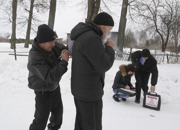I Novaja Rzhavka i Smolenskområdet foregik afstemningen udenfor ved en stemmeurne, der blev båret rundt. En vælger bruger sin kammerats ryg som skriveunderlag, da krydset skal placeres. 