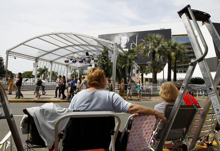 cannesfeber. Paparazzi og  nysgerrige flokkes tæt ved festivalens indgang, hvor den røde løber snart bliver lagt ud. 