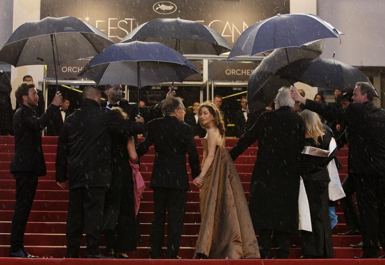 Regn. Den franske skuespiller Isabelle Hubbert ser sig tilbage, mens resten af holdet bag Michael Hanekes konkurrencefilm 'Amour' er på vej i firspring mod indgangen. 