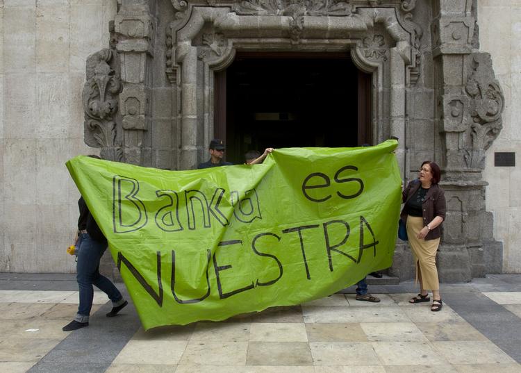 protest. En politibetjent holder vagt uden for en filial af Caja de Madrid/Bankia mens demonstranter går forbi med et banner med påskriften 'Bankia er vores'. 