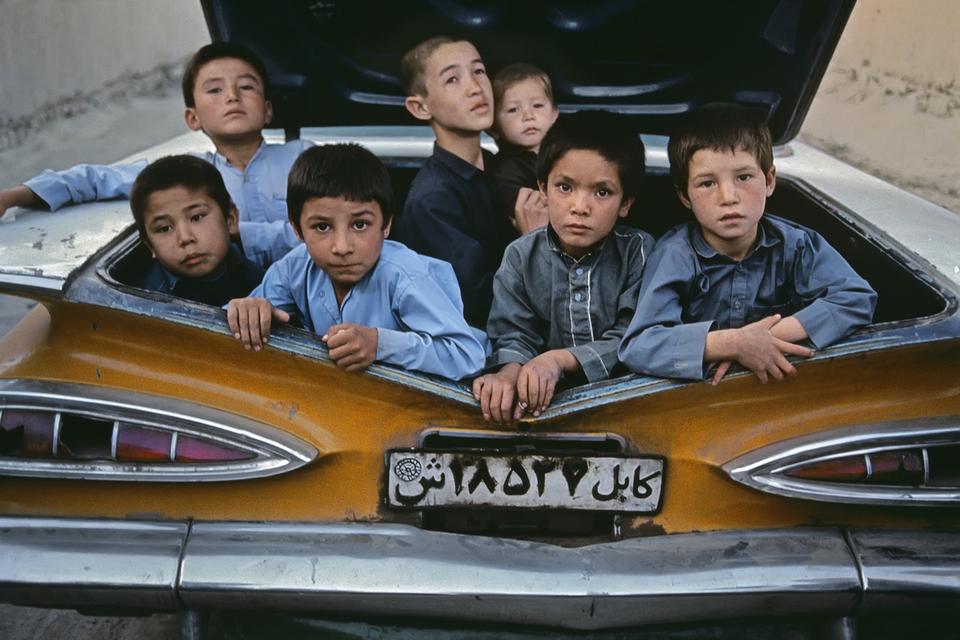 Drenge fra Kabuls gader 'ombord' i en gammel russisk bil, der er blevet bygget om til en åben taxi, hvor al ledig plads bruges til passagerer. 1992. 