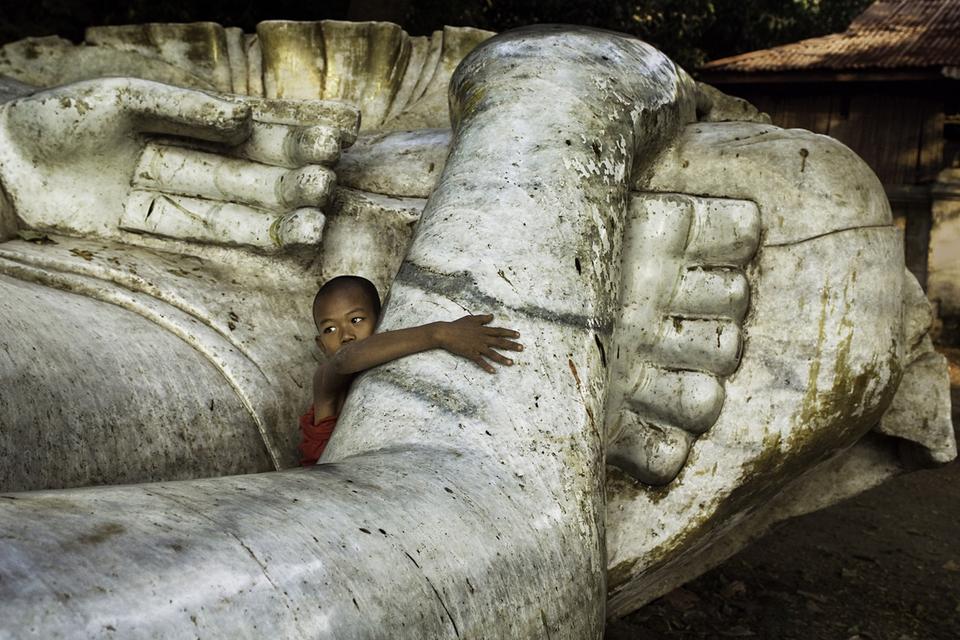 En meget lille munk holder om en meget stor Buddha-statue i Mandalay i Burma, 2008. 