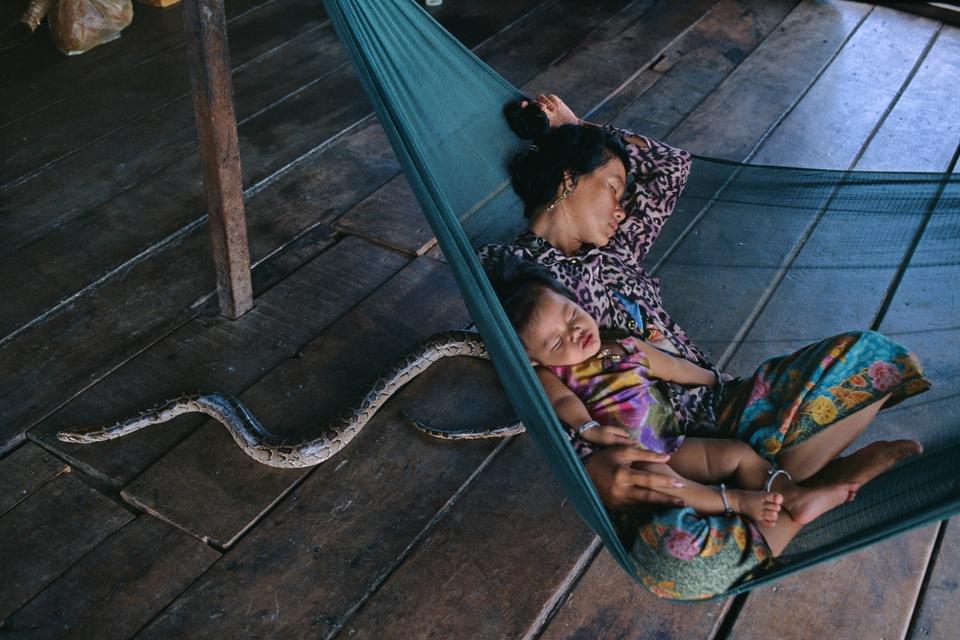 En mor og hendes datter hviler sig ombord på deres husbåd ved Cambodias største sø, Tonle Sap. Slangen bor på båden, og familien tjener penge på at lade sig fotografere sammen med den. 