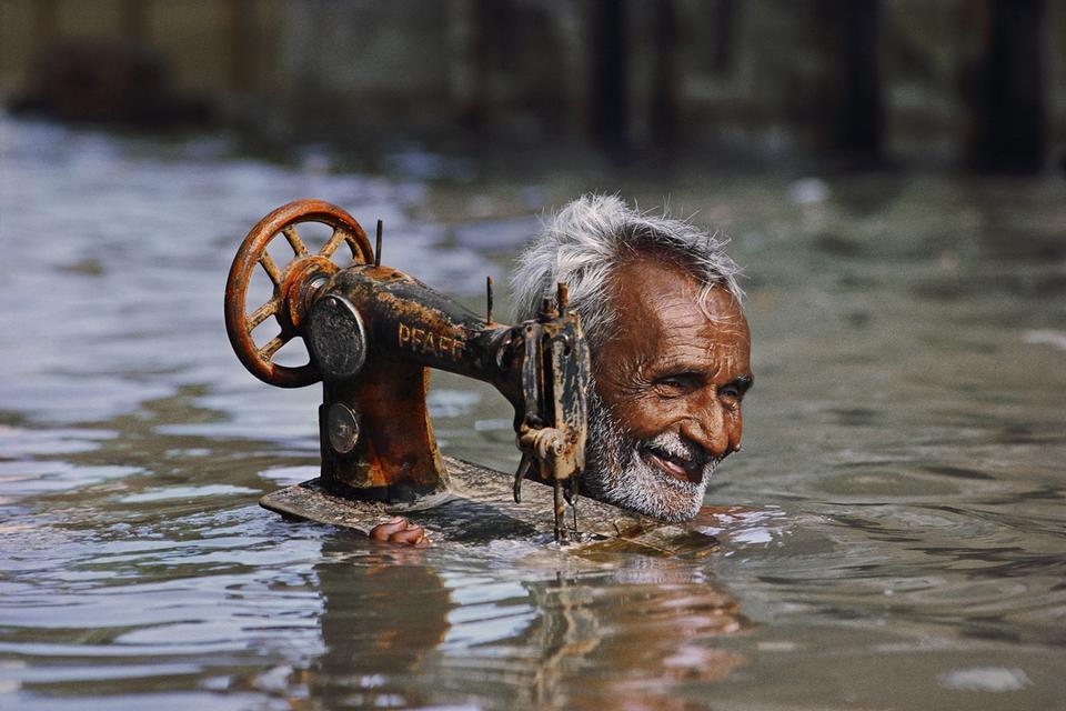 En skrædder bærer sit vigtigste arbejdsredskab gennem vandet fra monsunregnen i Porbandar i Indien, 1983. 