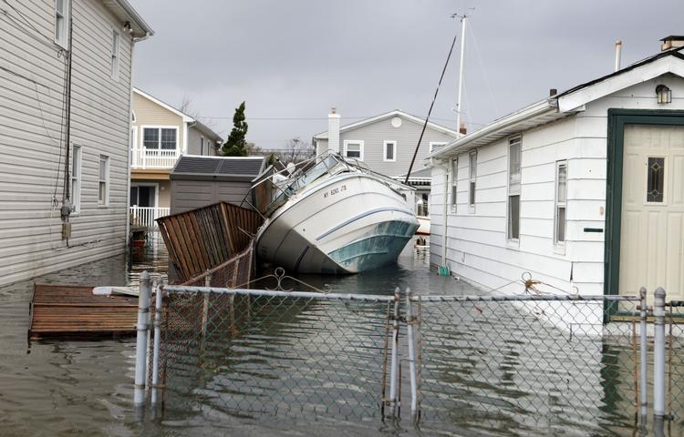 En sejlbåd ligger skyllet op mellem to oversvømmede huse i Lindenhurst, New York. 