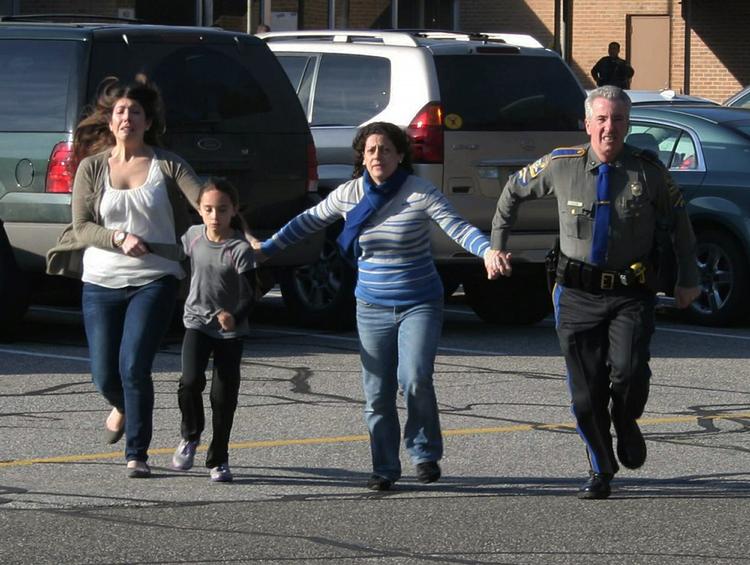 Flugt. En politimand fører tp kvinder og et barn væk fra gerningsstedet på Sandy Hook-skolen, hvor en gerningsmand har skudt tyve børn, seks voksne og til sidst taget sit eget liv. 