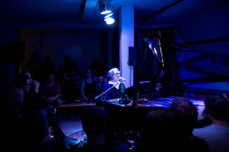 Blålys.  En kælder til en klaverbutik i København blev til en intim scene, da Jacob Bellens m.fl. indtog kælderens midte som et led i Frost Festival 2013.  Det blå lys er festivalens kendetegn. 