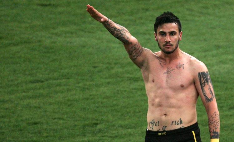 livstidskarantæne. AEK Athens midtbanespiller Giorgos Katidis løfter højre arm til en nazilignende hilsen ud mod publikum efter sin scoring mod Veria. 