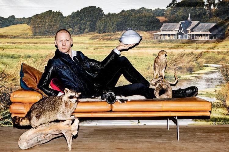 HVERDAGSLIV. Den daglige ramme er afgørende for Jim Lyngvild, her på briks fra BoConcept, foran plakat af hans egen borg, i jeans og jakke fra G-Star med mågestelterrin, vaskebjørn, musvåge og nyindkøbt Hasselblad-kamera. Foto: Daniel Hjorth 