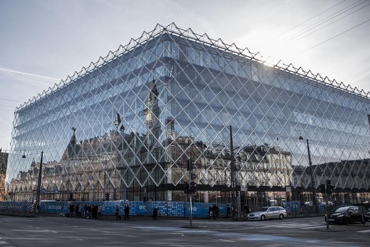 Facaden. Langs Vesterbrogade forsvinder glassets store blanke flade helt i spejlinger af himlen. Der er intet relief i facaden, der holder oplevelsen af huset fast på stedet. 
