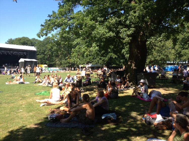 Havefest. Stemningen er afslappet og publikum slapper af i solen. I aften, når de store kunstnere går på scenen, vil pladsen for de to scener være fyldt med mennesker. 